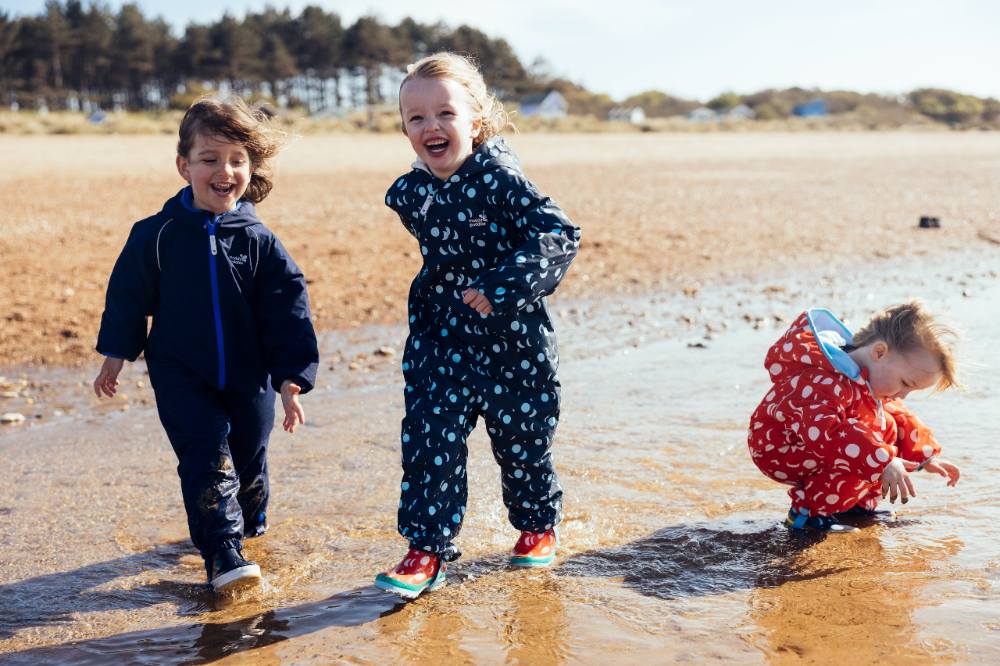 Three children stood on beach wearing Muddy Puddles outerwear