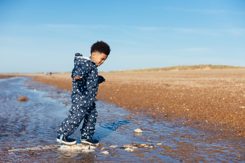 Boy paddling in the sea wearing Muddy Puddles outerwear