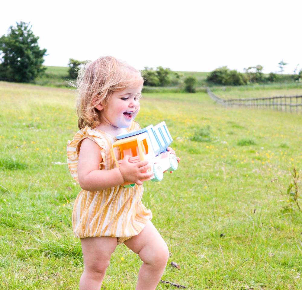 Girl walking in a field carrying a toy truck 