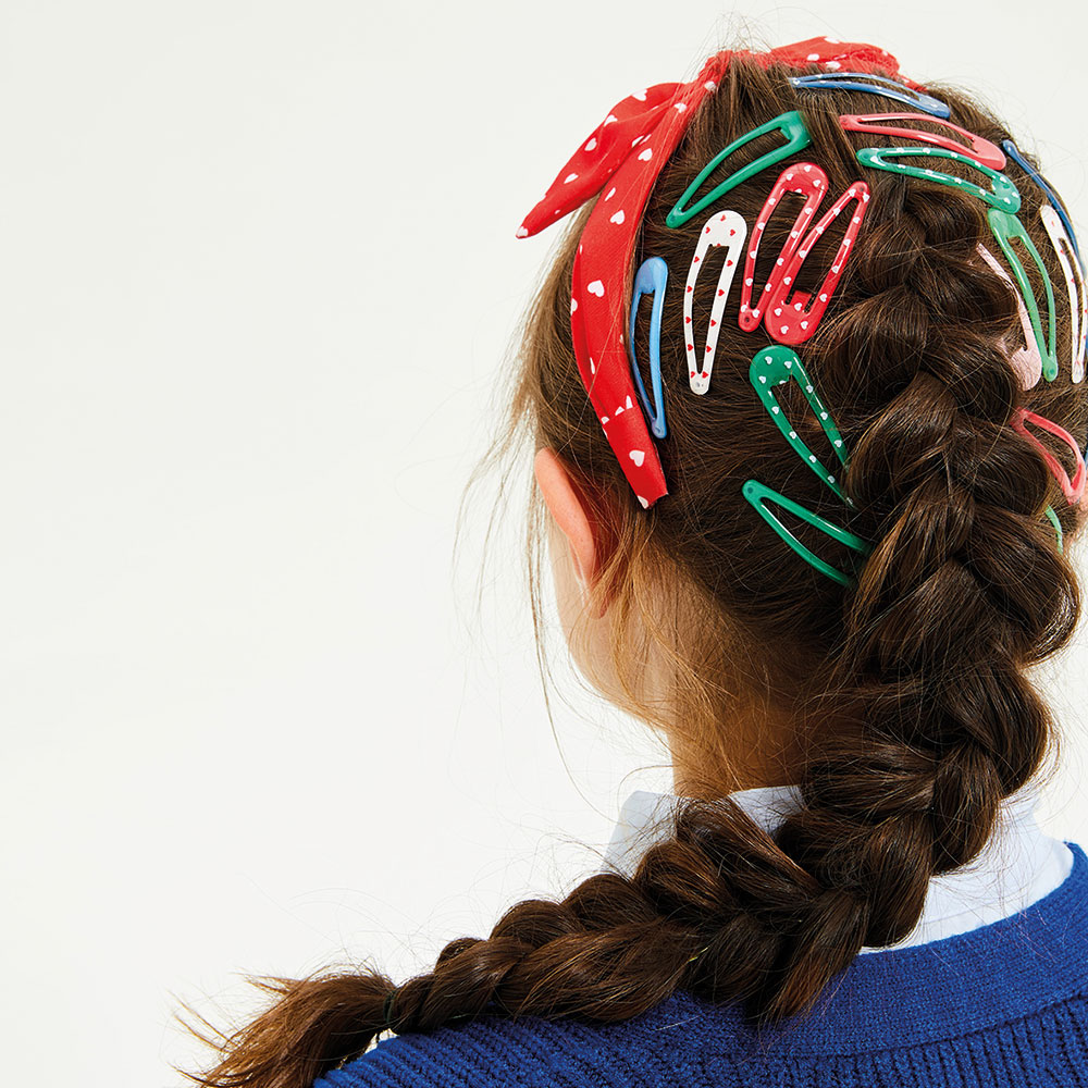 Back of a girl's head with long brown hair covered in school hair clips and a hairband
