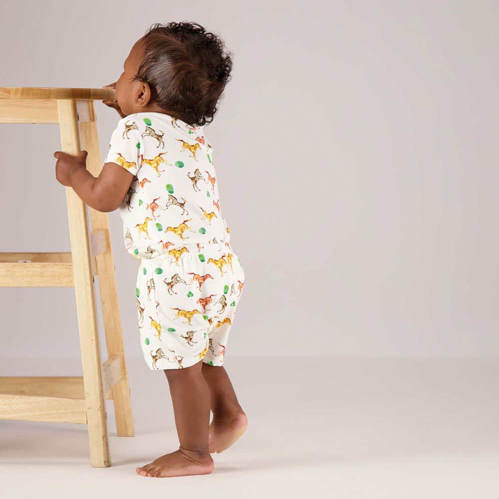 Baby wearing shorts and a T-shirt holding onto a wooden stool