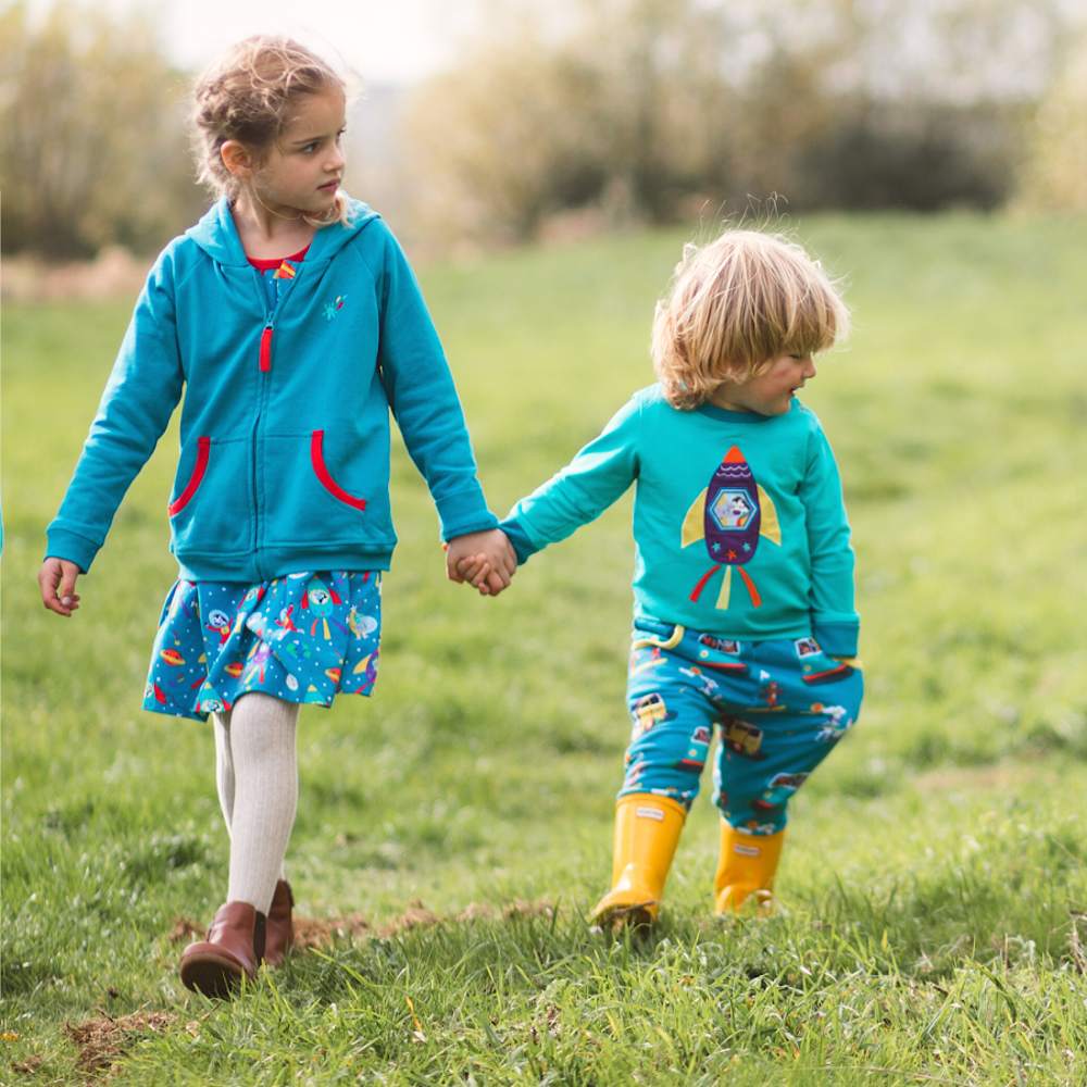 Two children walking in a field holding hands wearing the Christmas Collection by Ducky Zebra