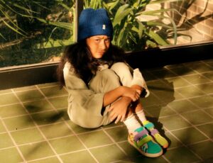 Child wearing a blue hat sat on a green tiled floor wearing Dulis Shoes