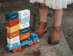 Childs legs stood by a blue wooden truck with wooden blocks stacked on it