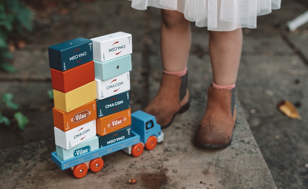 Childs legs stood by a blue wooden truck with wooden blocks stacked on it