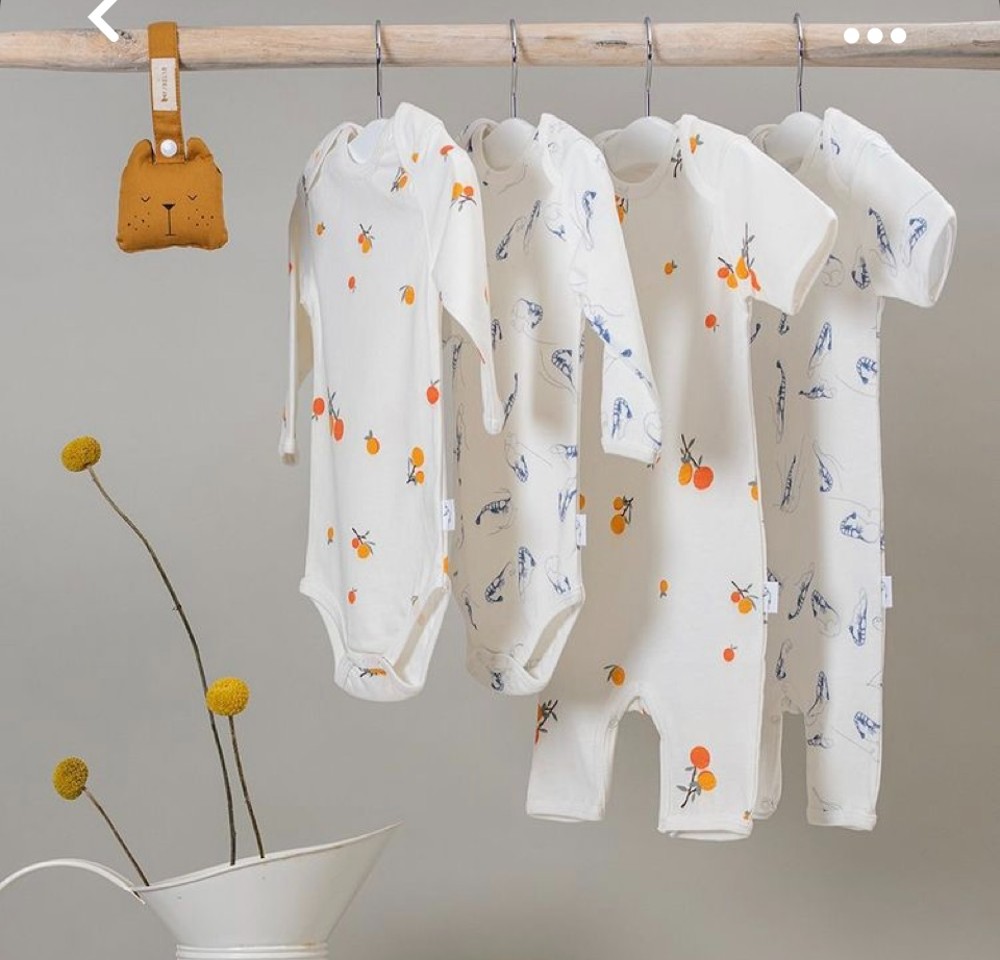 Four babywear garments and a baby toy hung on a wooden rail