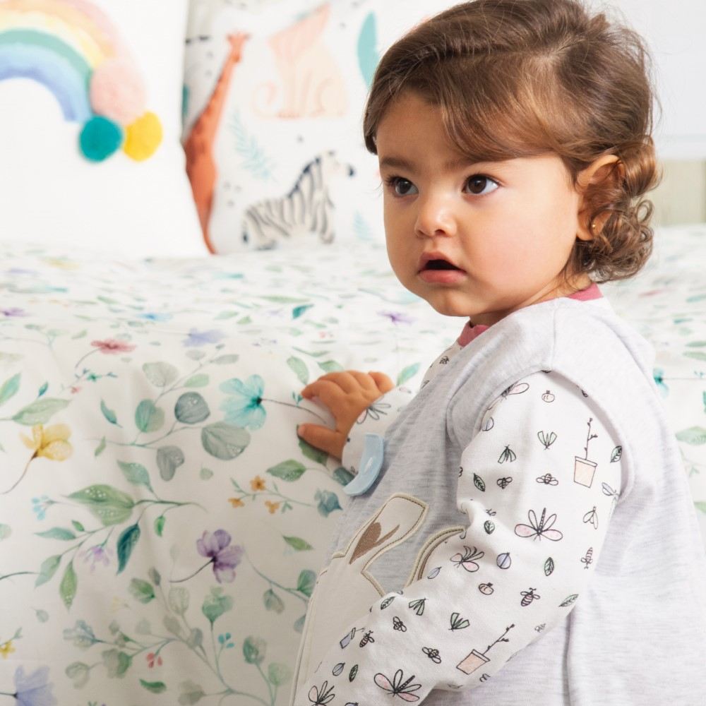 Child stood by a bed decorated in cushions wearing Plumas nightwear