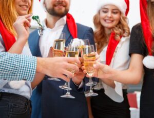 Four people dressed in Christmas hats and raising champagne glasses