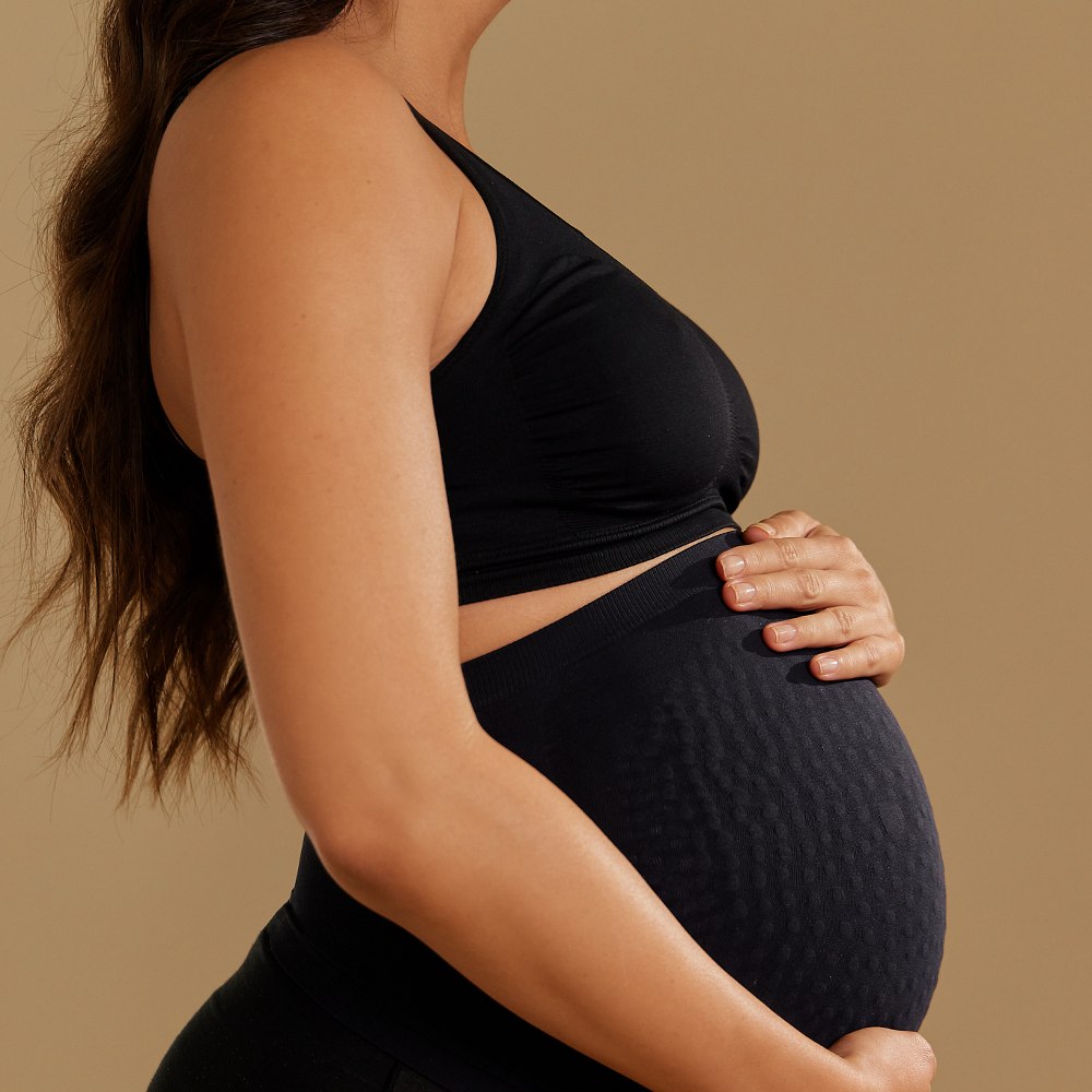 Side shot of a pregnant woman holding her bump wearing Secret Saviours
