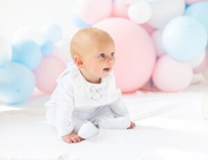 Baby sat on the floor in front of pastel coloured balloons