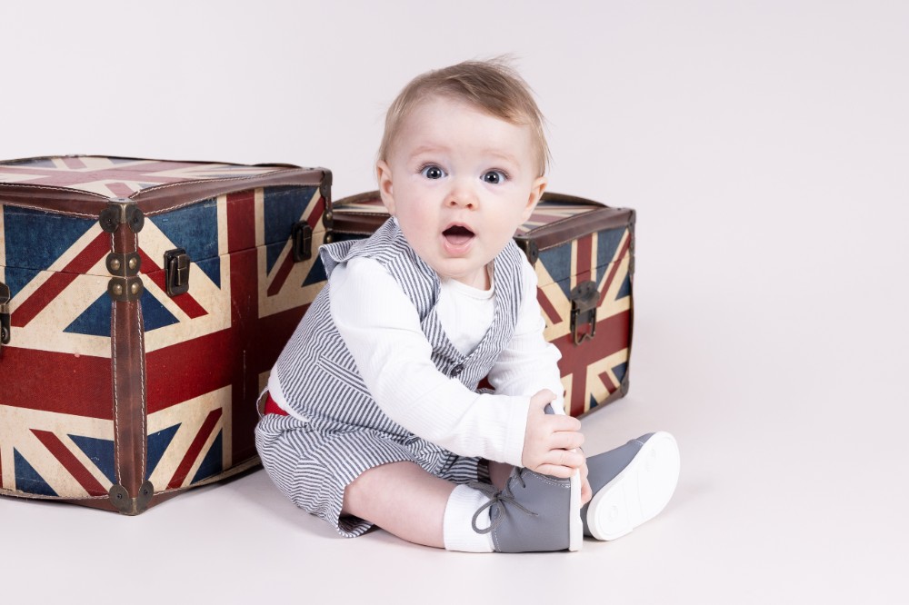 Toddler sat in front of Union Jack boxes wearing grey boots by Early Days