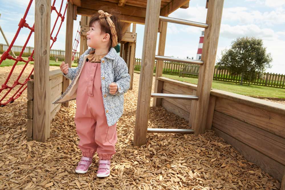 Girl stood outside under a wooden climbing frame wearing pink dungarees and Start-Rite Shoes 