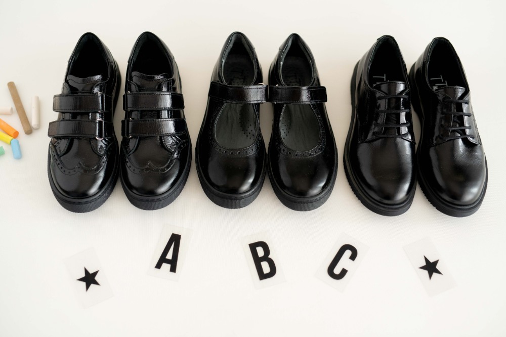 Black school shoes by TT Kids lined up on a white background with the letters A B C