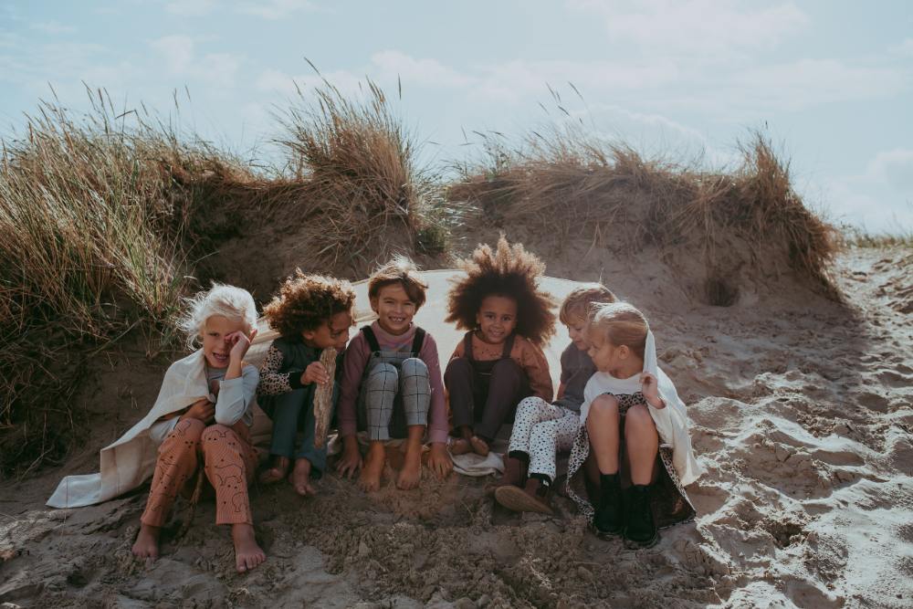 Children sat on a sand dune wrapped in blankets wearing clothing from A Moment of Calm collection by Turtledove London