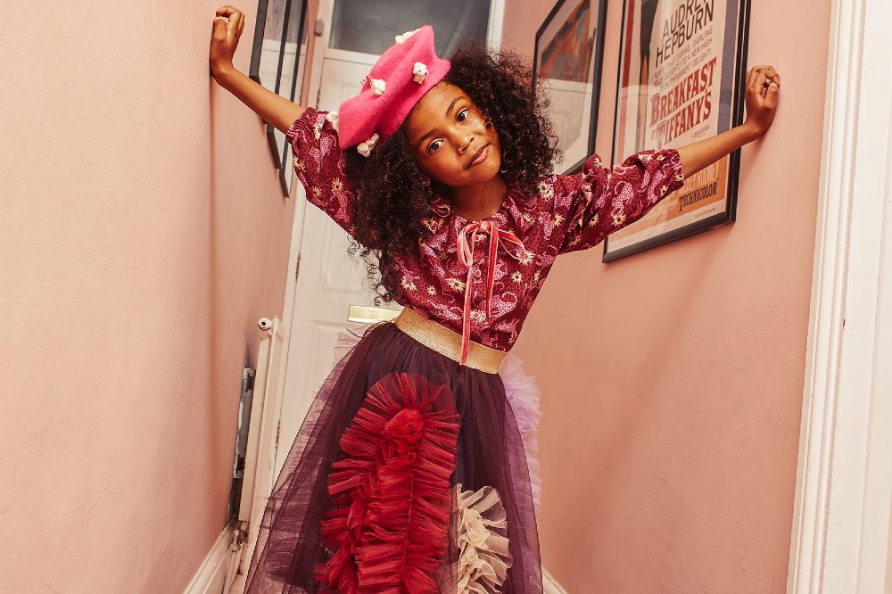 Young girl stood in a pink hallway wearing a pink hat, patterned top and a red and purple frilled skirt promoting the Pro-Seller Service by dotte
