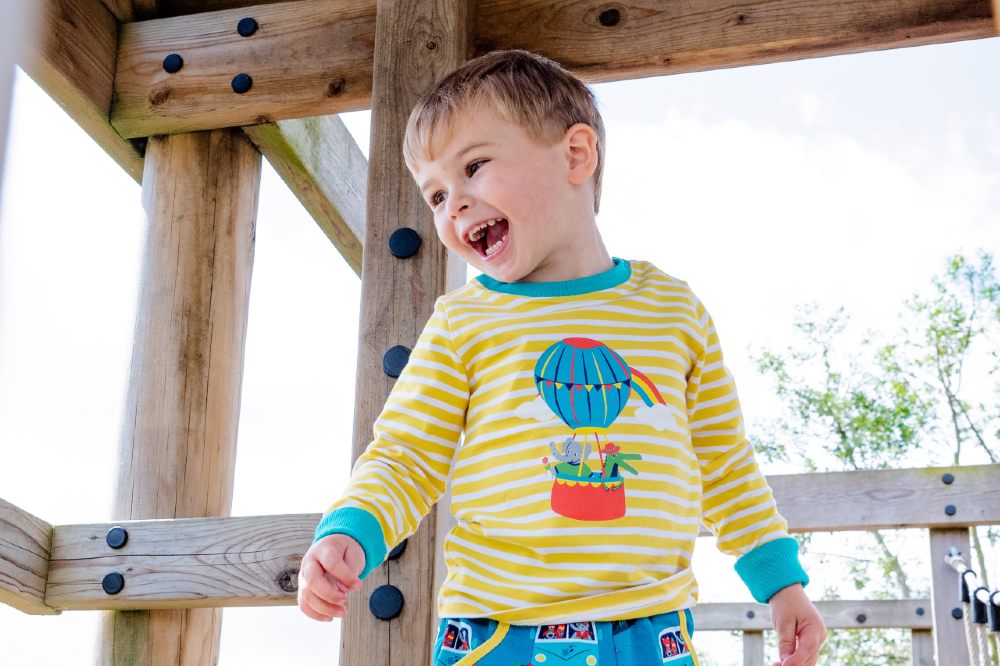 Boy stood beneath a wooden climbing frame wearing a yellow striped top and blue trousers by Ducky Zebra