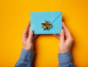 Hands holding a blue envelope containing a gift card against a yellow background