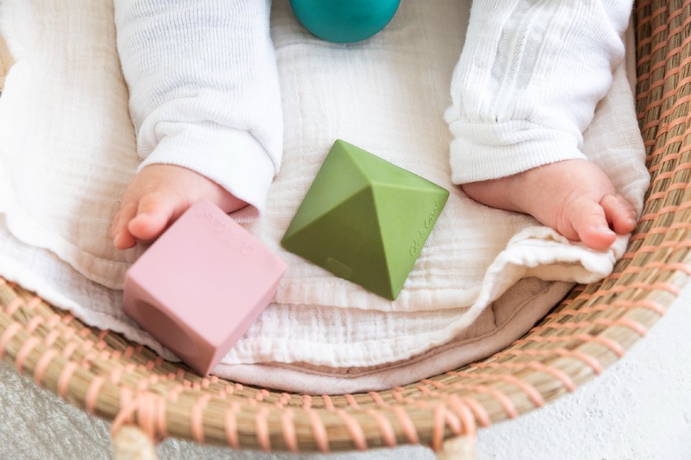 A baby's legs in white trousers sat in a basket with toys from the Oli & Carol x Bauhaus Movement collaboration