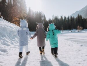The back of three children walking in the snow wearing Roarsome Parkas