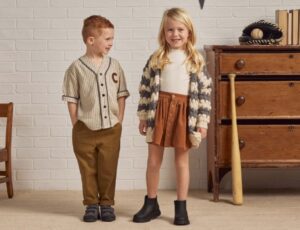 Two children stood in a room beside a wooden dresser and chair