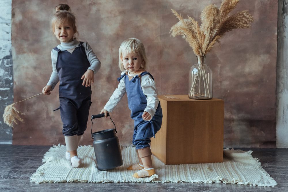 Two children stood on a white rug wearing blue dungarees