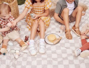 Children sat outside on a picnic blanket wearing shoes from the Bobux Dare to Roam collection