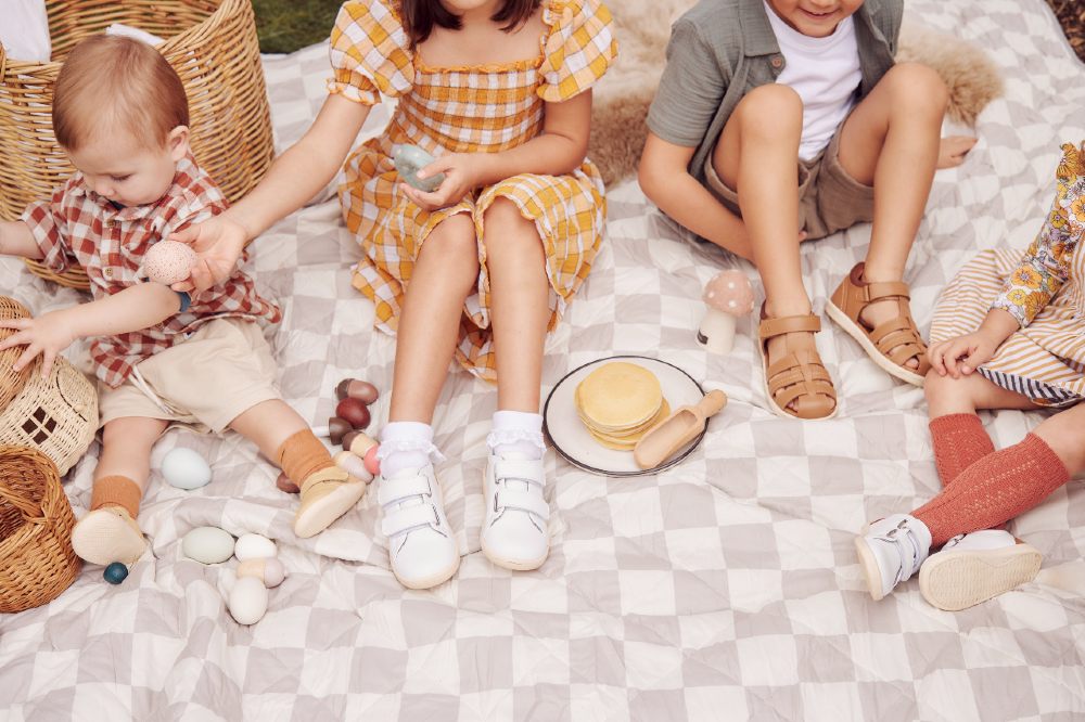 Children sat outside on a picnic blanket wearing shoes from the Bobux Dare to Roam collection