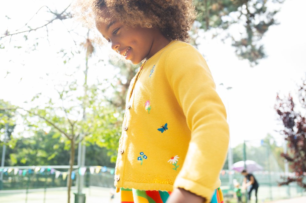 Young girl stood outside wearing a yellow cardigan by Frugi