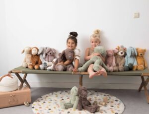 Two young girls sat on a bench surrounded by soft toys by Happy Horse