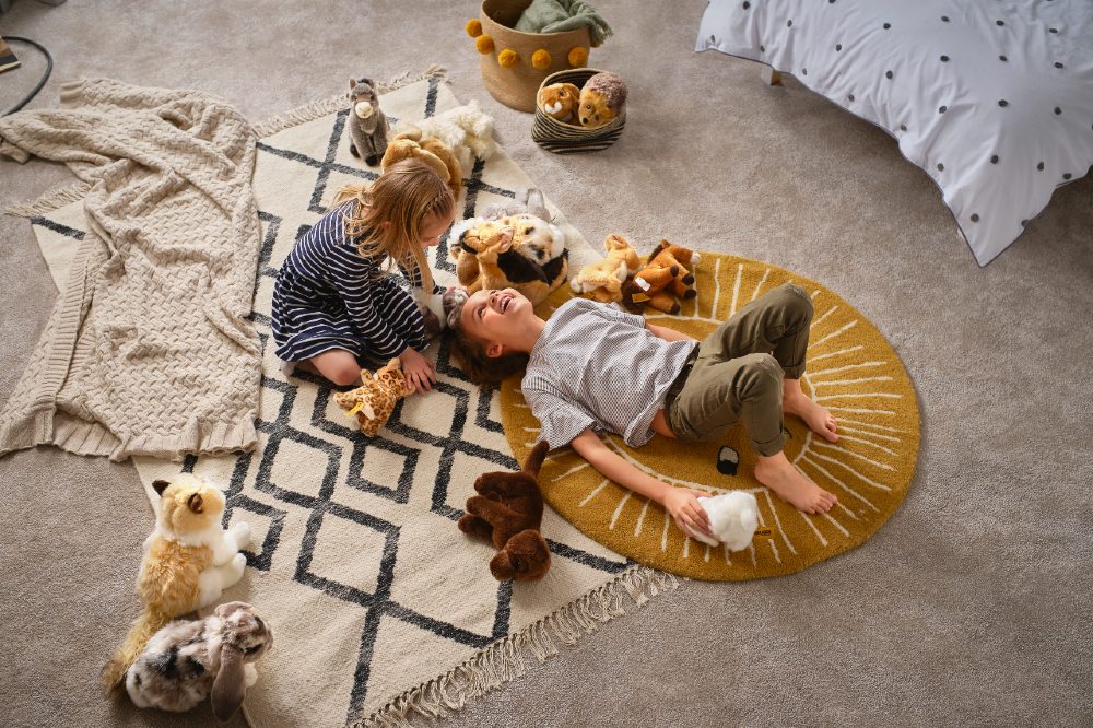 Two children sat on rugs on the floor surrounded by toys