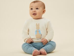 Baby sat on the floor wearing blue leggings and a Peter Rabbit by MORI top
