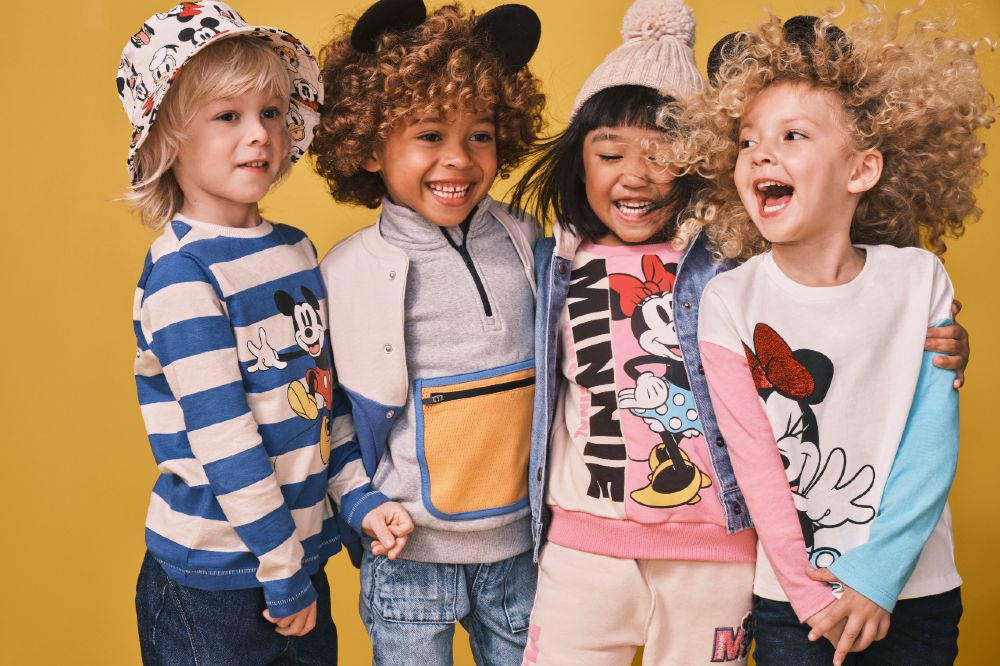 Four young children stood against a yellow background wearing the Disney collection by M&S Kids