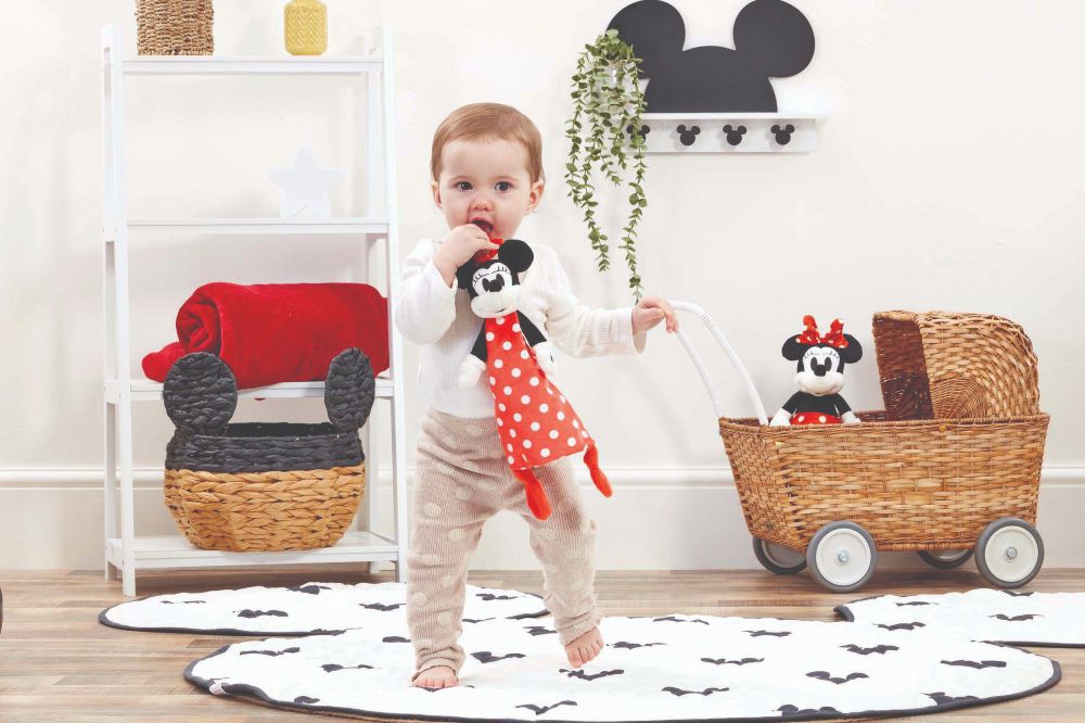 Young child stood in a room holding a Minnie Mouse doll by Rainbow Designs