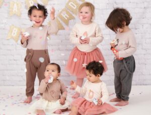 Five young children wearing Tiny Victories childrenswear throwing confetti with a birthday banner in the background