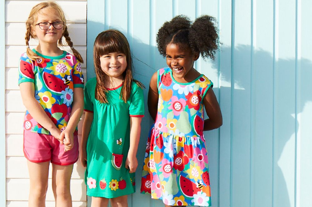 Three young girls stood in front of a pale blue wood panelled wall wearing Toby Tiger clothing