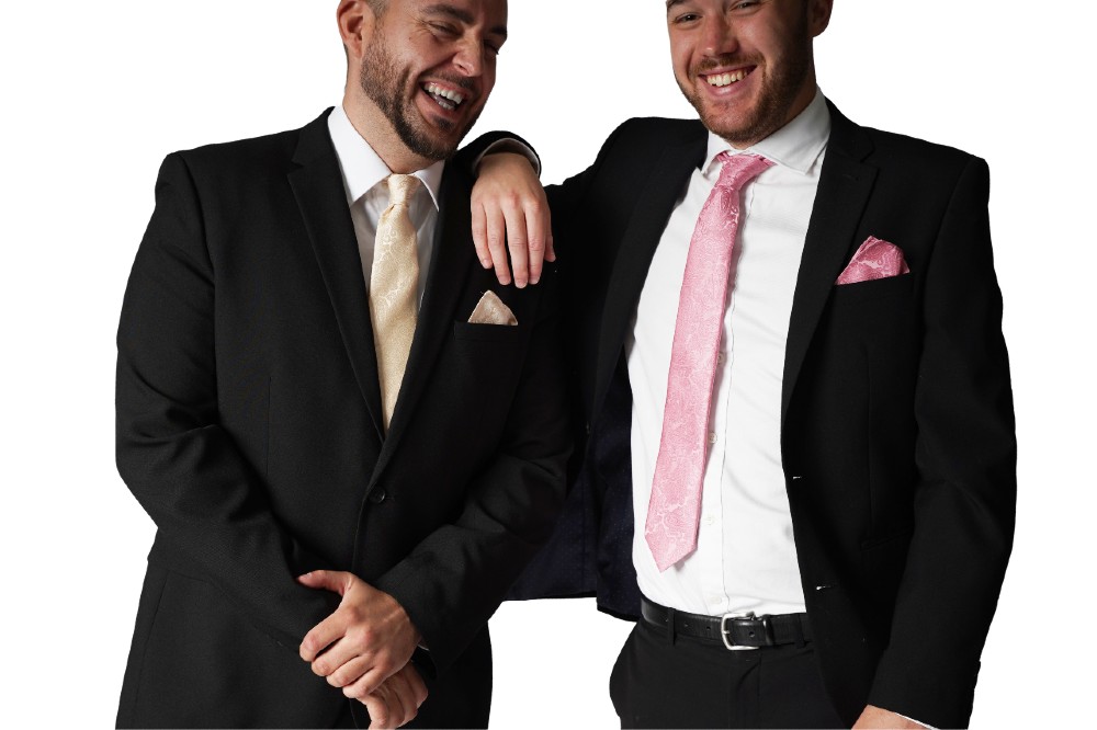 Two men wearing black suits and ties and pocket squares from the William Turner Occasion Wear range