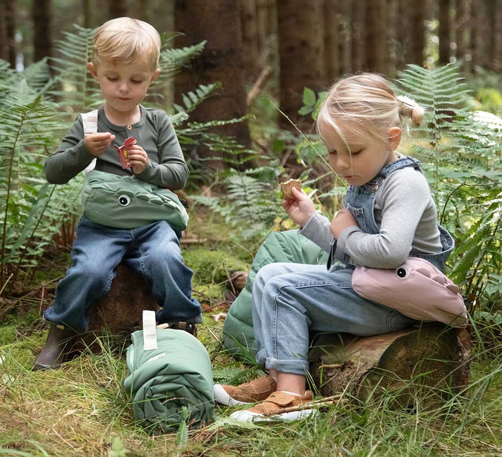Boy and girl sat down in woodland wearing cross-over bags