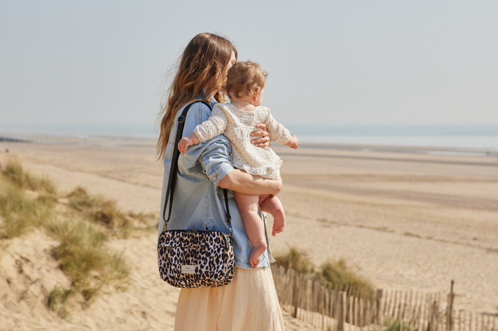 Woman stood on a beach holding a baby and carrying a Finssøn changing bag on her shoulder