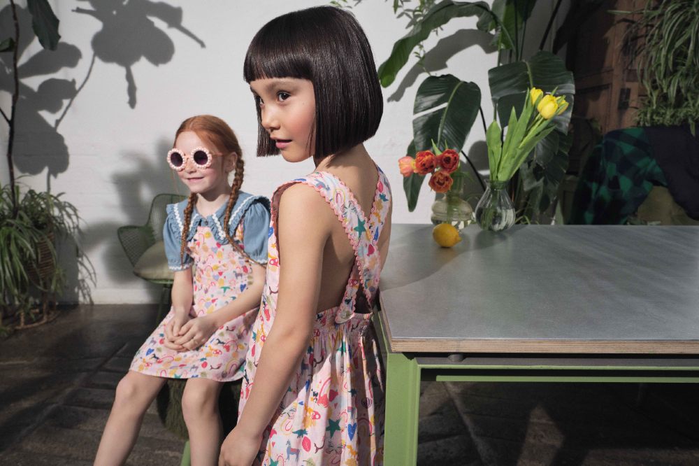 Two girls stood by a table and plants wearing dresses by Stych