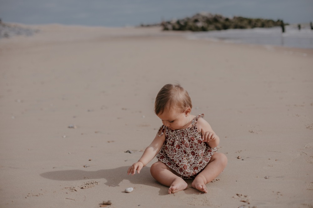 Young child sat on a beach wearing a romper by The Small Folk