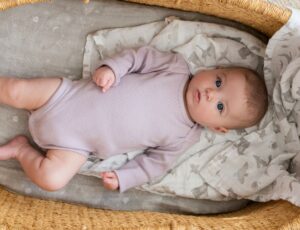 Baby in a Moses basket lying on a muslin blanket by aden + anais