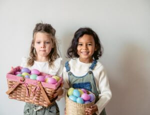 Two young girls holding baskets containing different coloured Easter eggs