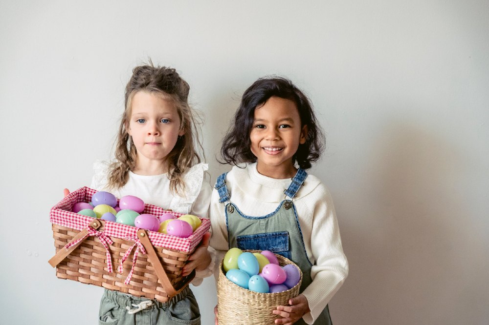 Two young girls holding baskets containing different coloured Easter eggs