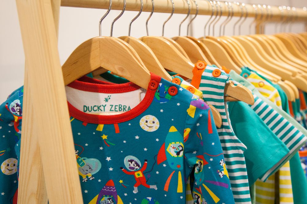 Brightly coloured children's clothes hung on a wooden rail on a stand at INDX Kids