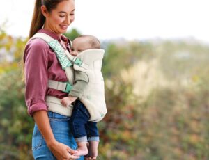 Women carrying a young child in the Infantino Flip 4-in-1 Nature & Nurture Convertible Carrier