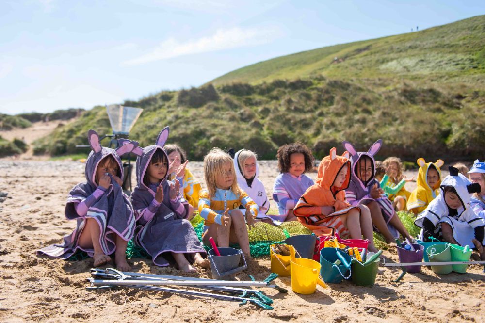 Children sat on a beach wearing hooded towels by Roarsome