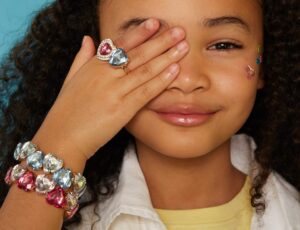 Young girl holding her hand up to her eye wearing a bracelet and ring by Super Smalls
