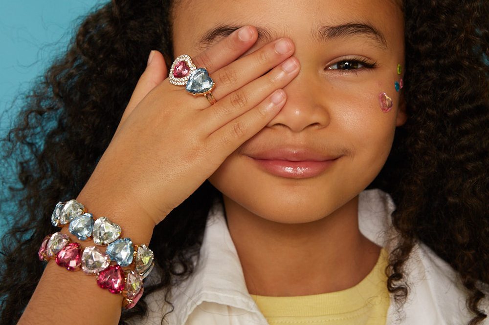 Young girl holding her hand up to her eye wearing a bracelet and ring by Super Smalls