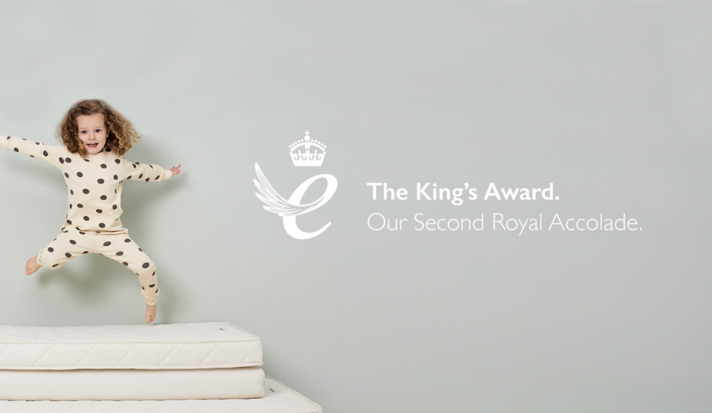 A young girl jumping on a mattress next to the King's Award Logo
