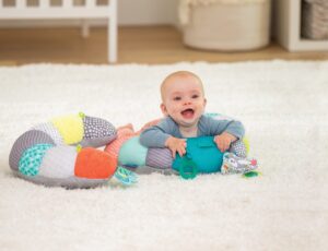 Young baby sat on the floor supported by a colourful pillow